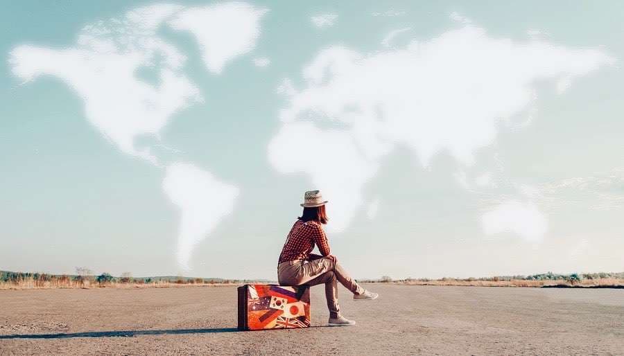 Life-Path-5-the-Adventurer Women Traveler Sitting on case on Airfield, clouds forming map of the world