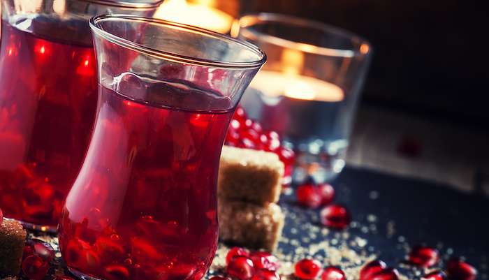 Festive red hot drink with pomegranate on an old wooden table against a background of burning candles, selective focus Autumnal Equinox Pomegranate Tea Recipe To Welcome The Change Ahead
